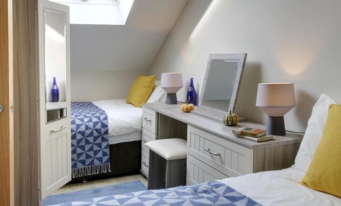 Bright attic twin bedroom with a skylight, blue patterned throws, and a dressing table with mirror and lamps.